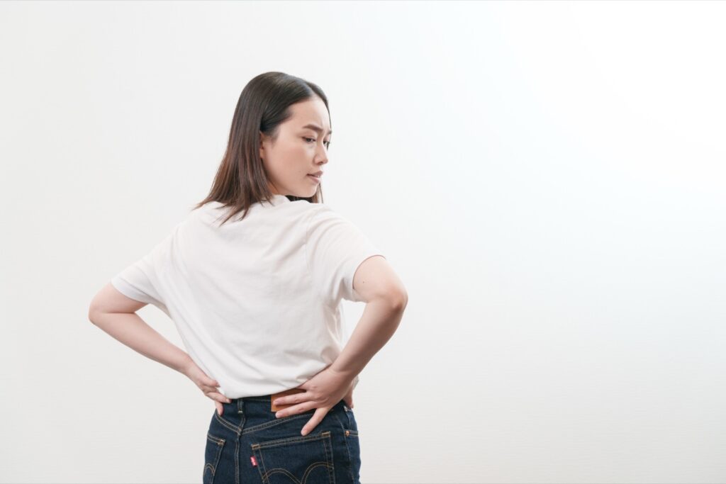 腰に手を当てて、つらそうにしている女性
