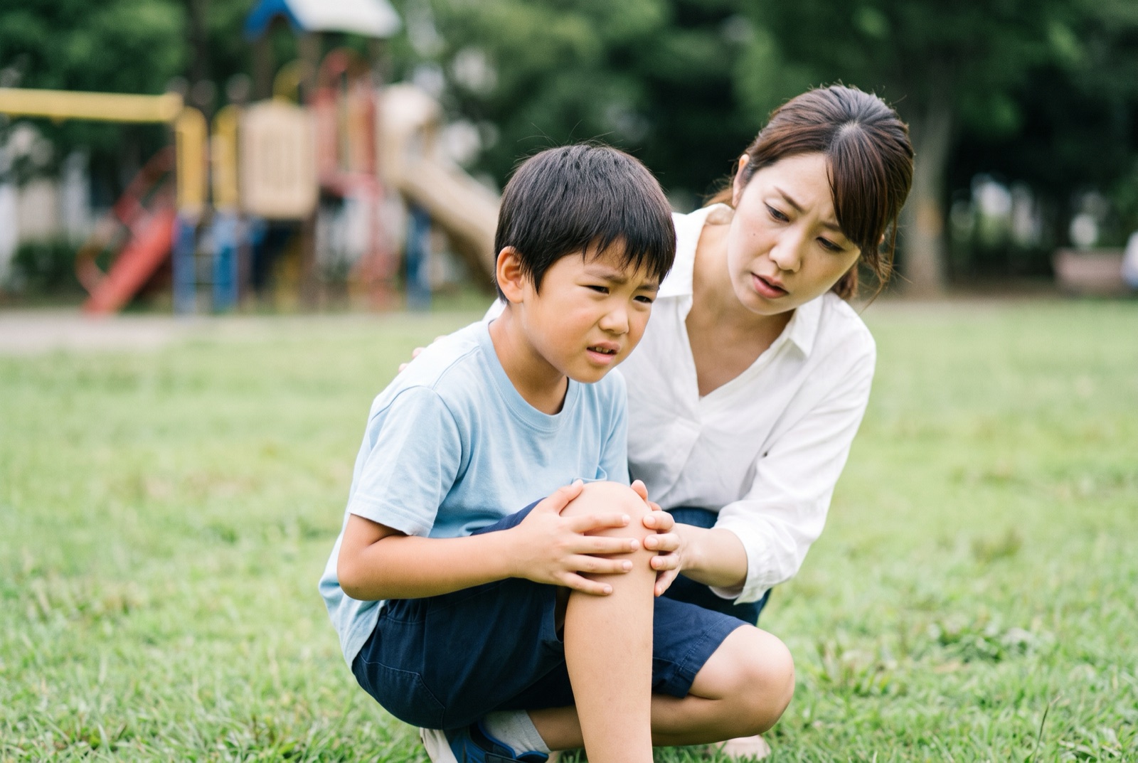 公園で転んで膝を押さえている子どもと、そばに寄り添う母親
