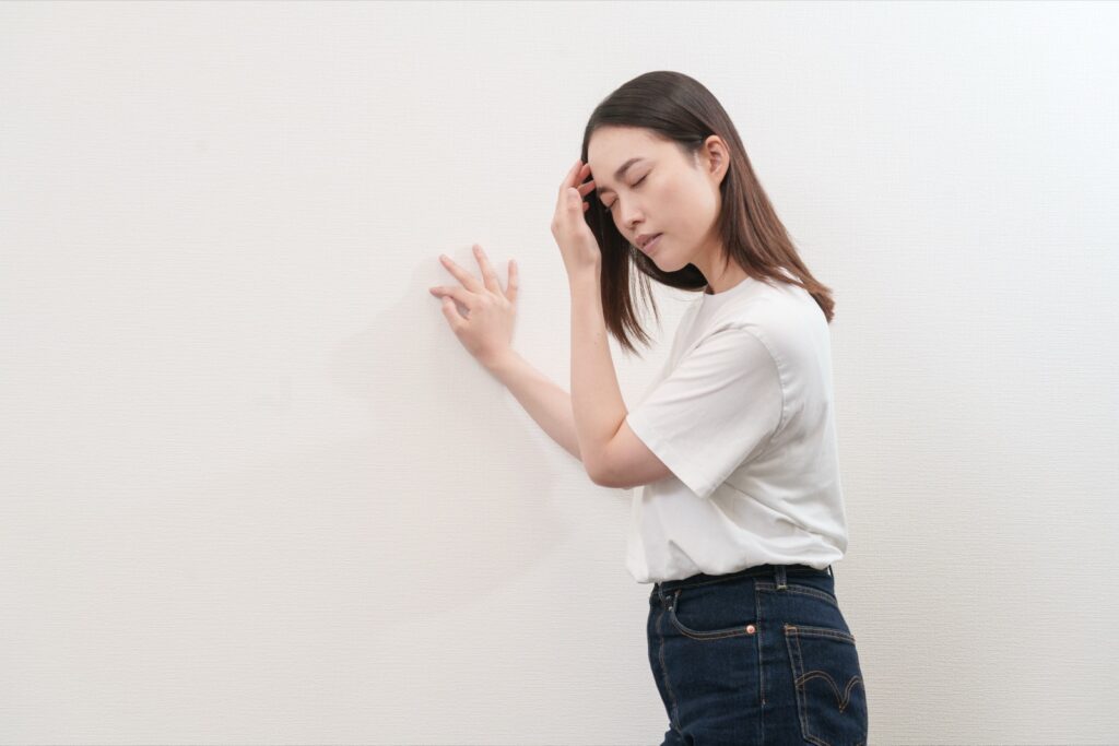 壁に手をついて、頭の重さを感じている女性