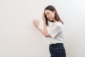 壁に手をついて、頭の重さを感じている女性