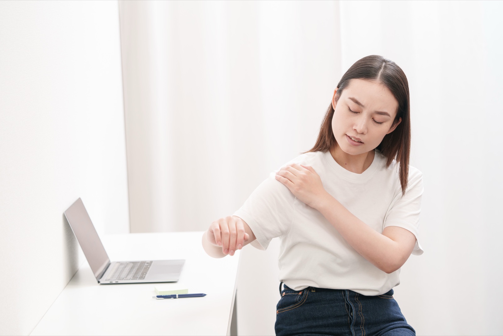 デスクワークの途中で肩と腕を押さえる女性