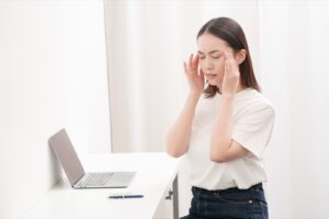 デスクワークの途中でこめかみを押さえる女性