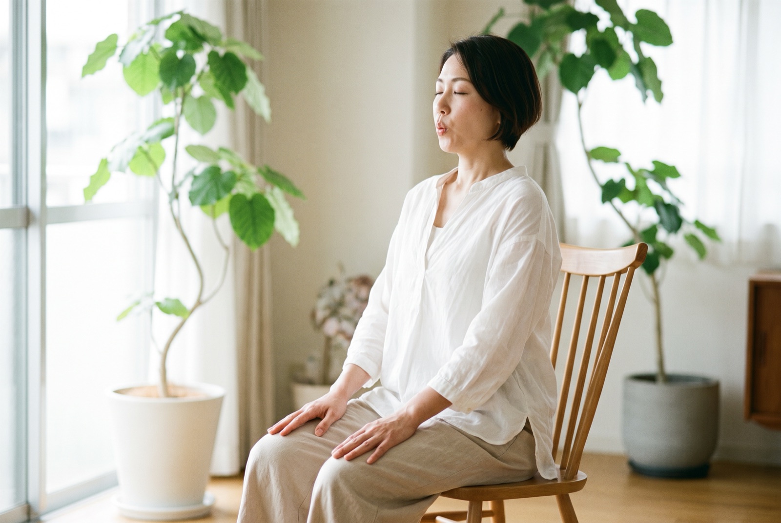 椅子に座って、口をすぼめてゆっくり息を吐いている女性