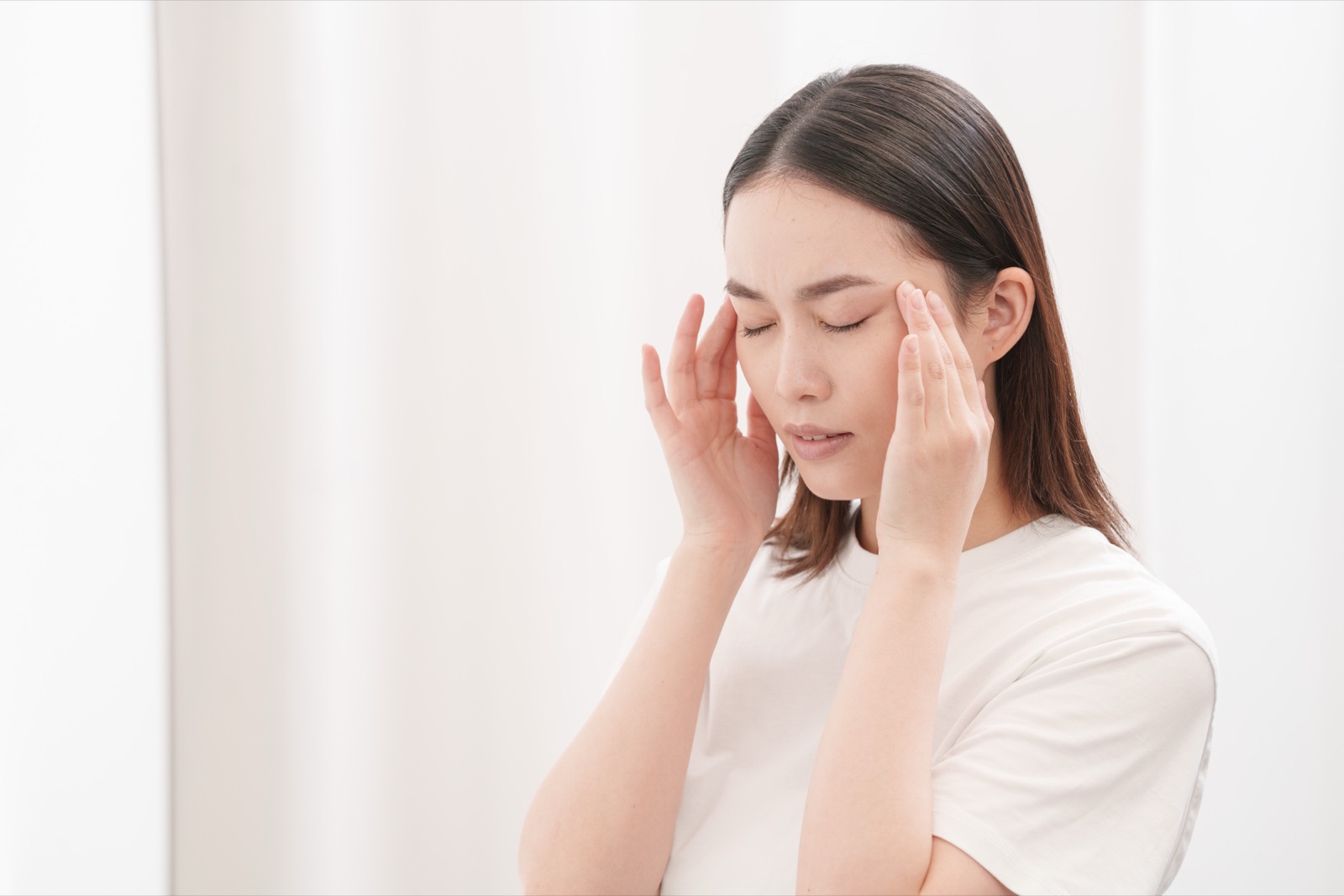 デスクワークの途中でこめかみを押さえる女性