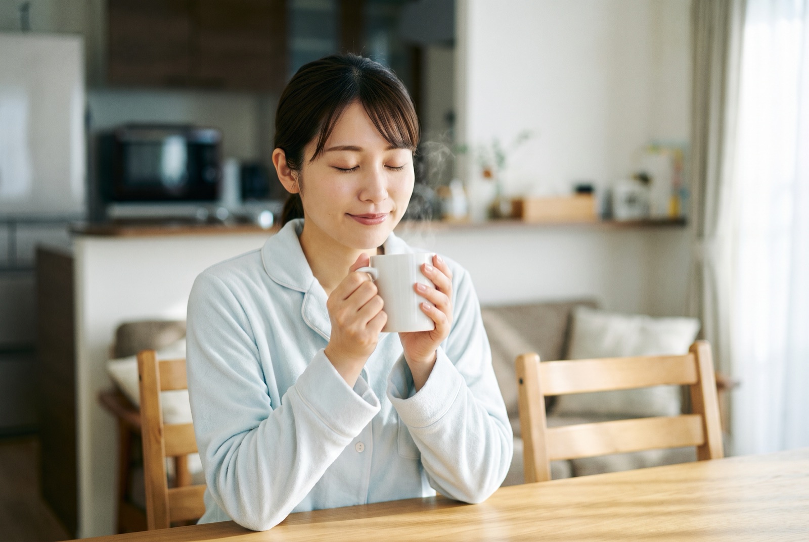 白湯の入ったマグカップを両手で包むように持ち、手のひらの温かさを感じている女性