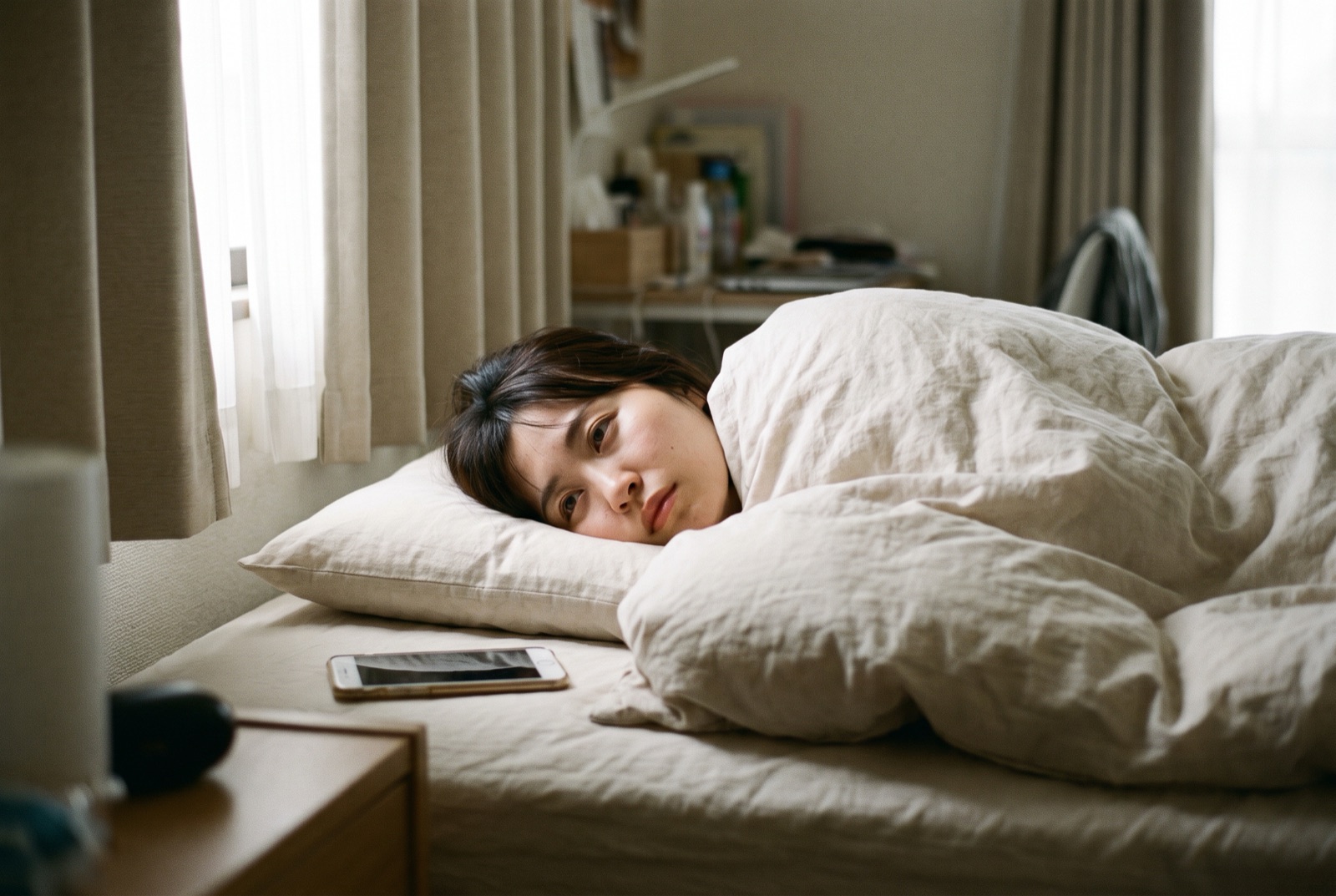 休日の昼、布団にくるまったままベッドで横になっている女性