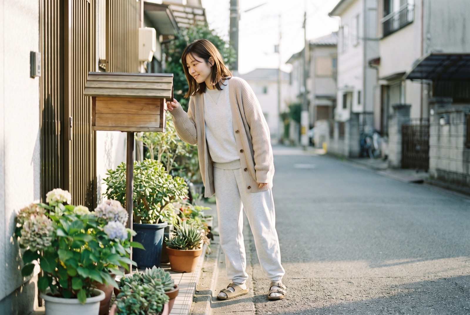 部屋着のまま玄関先に出て、郵便受けをのぞいている女性