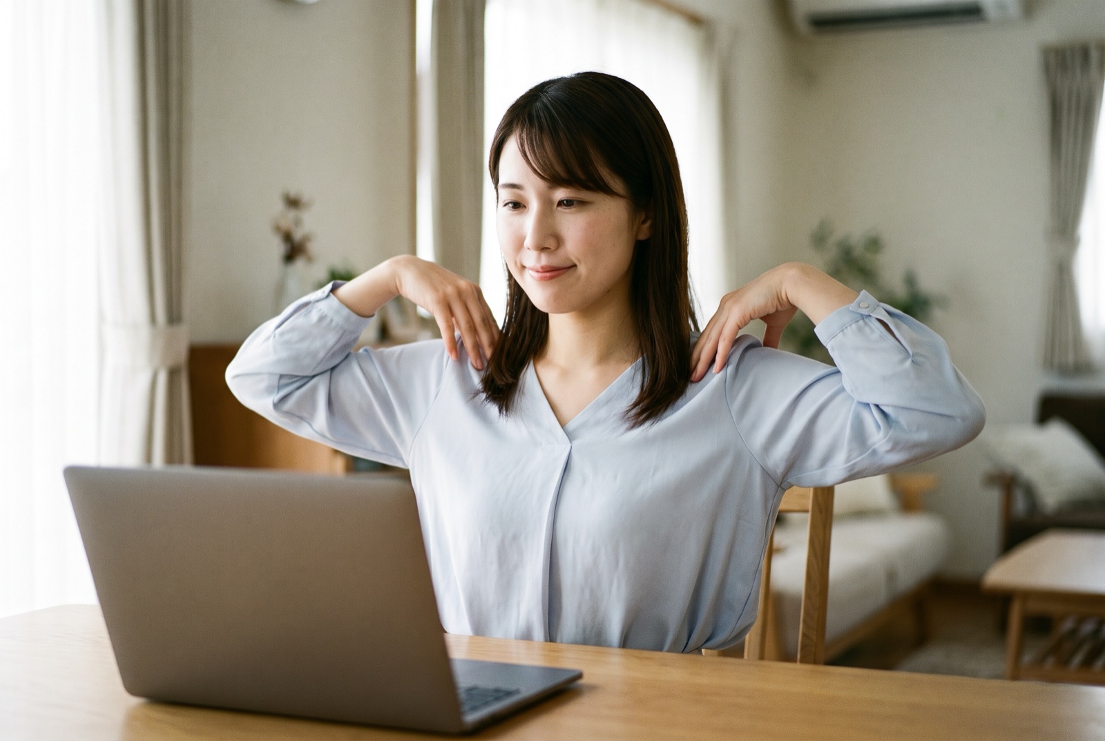 椅子に座り、両手の指先を肩に置いて、ひじで大きく円を描いている女性