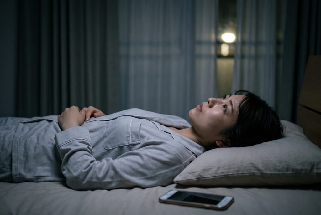 暗い寝室で、布団に入ったまま目を開けて天井を見つめている女性