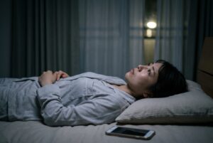 暗い寝室で、布団に入ったまま目を開けて天井を見つめている女性
