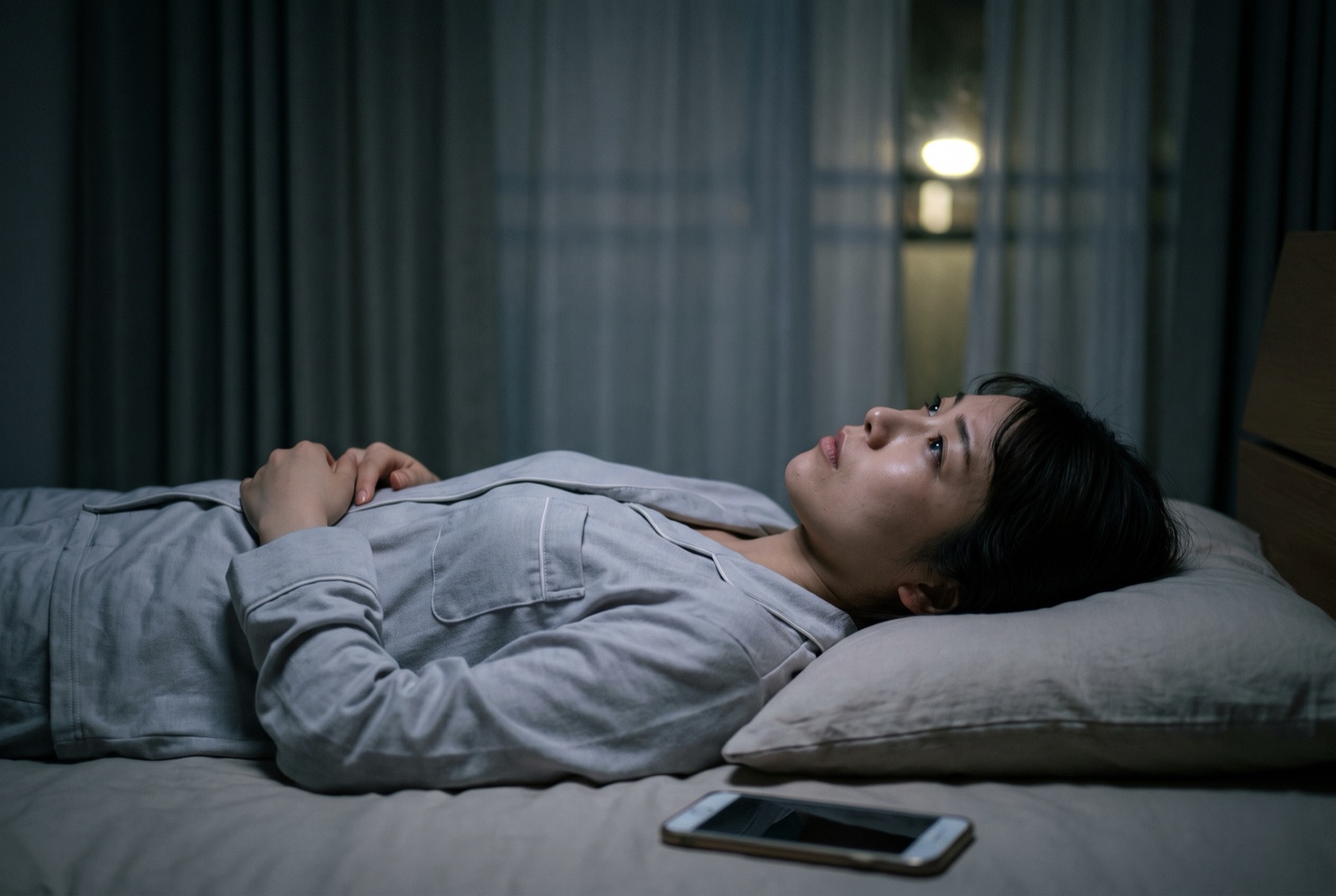 暗い寝室で、布団に入ったまま目を開けて天井を見つめている女性